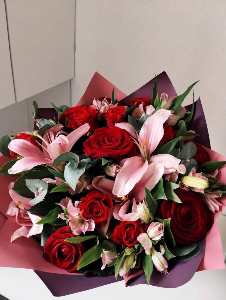 Ramo de rosas rojas y lirios rosados con follaje verde